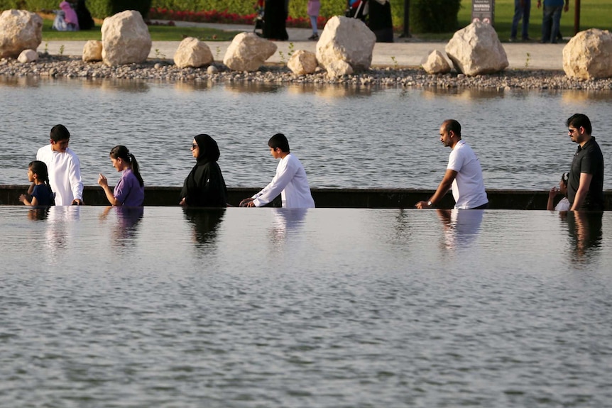 Visitors cross an ornamental lake in Dubai's Koranic Park on a path that is partly submerged below the water line.