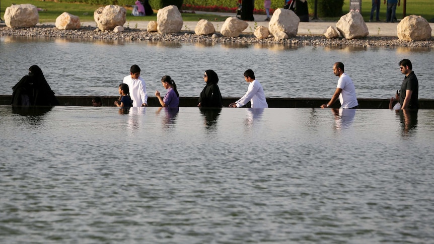 Visitors cross an ornamental lake in Dubai's Koranic Park on a path that is partly submerged below the water line.