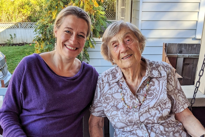 An old and young woman posing for a photo. Sitting down, smiling and looking at the camera.