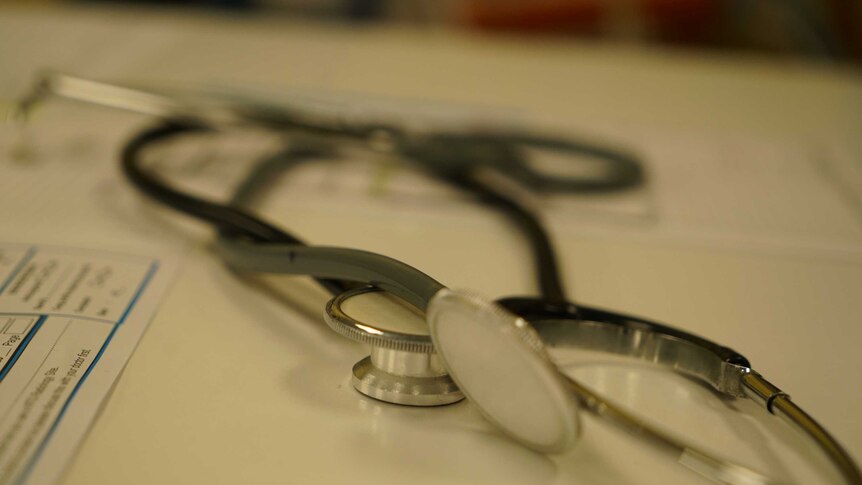A close up shot of a stethoscope sitting on a white bench and paper work out of focus underneath