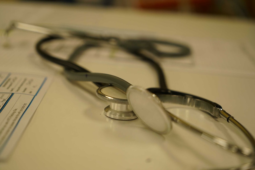 A close up shot of a stethoscope sitting on a white bench and paper work out of focus underneath