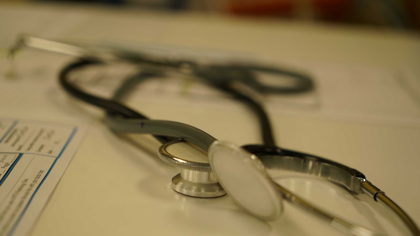 A close-up shot of a stethoscope sitting on a white bench and paper work out of focus underneath.