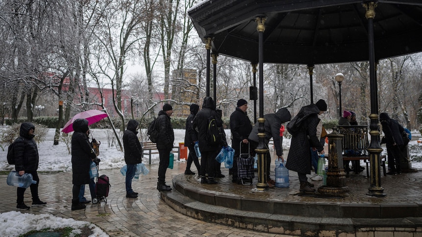 People carrying plastic bottles wait outside in line to collect water.