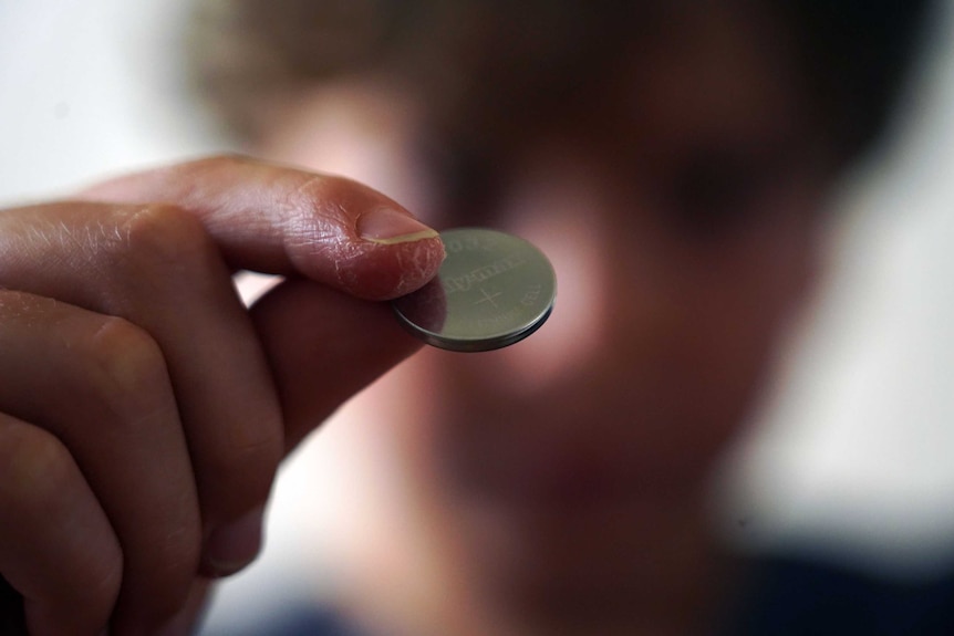 A close up view of a lithium button battery held by a seven-year-old boy.