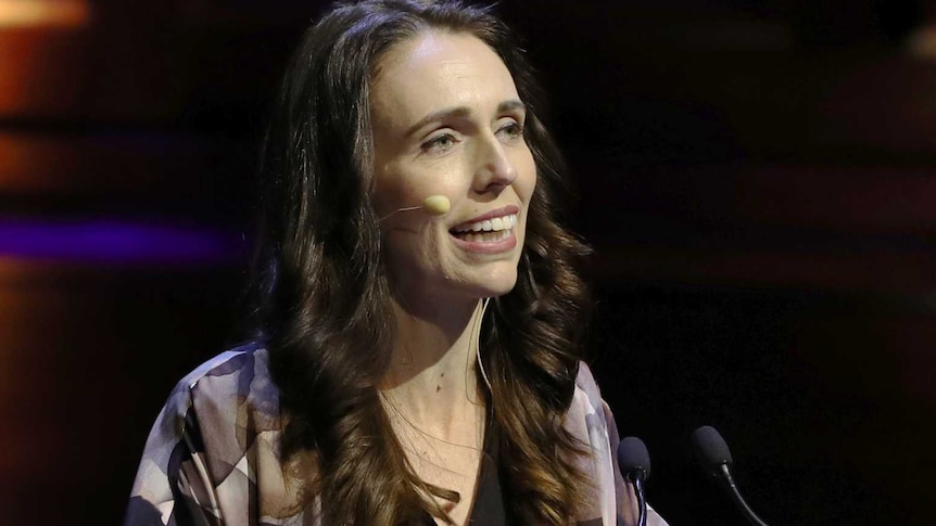 Jacinda Ardern wearing a purple top speaking at a lectern.