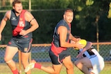 An Aboriginal footy player holds onto a ball planning his next move while a teammate approaches. 