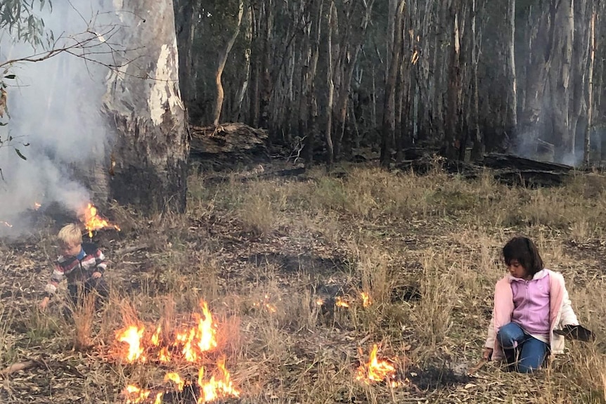 Two children sitting in bushland learning cultural burning techniques.