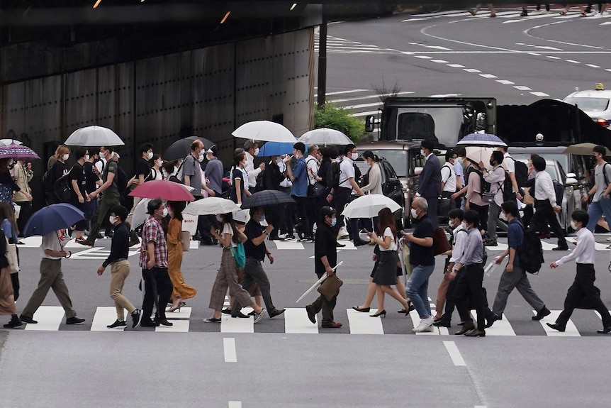 people wearing masks cross two pedestrian crossings with some people holding umbrellas