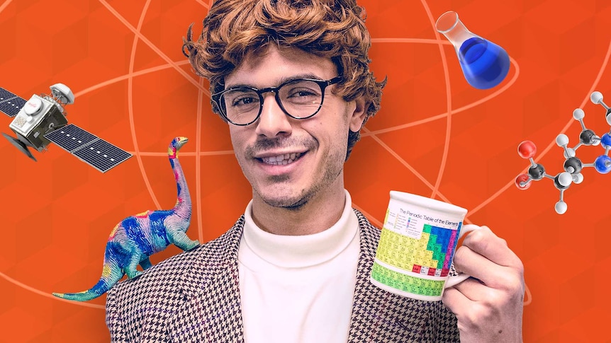 Jack poses in a wig and tweed jacket while holding a periodic table mug in one hand and other sciencey objects float around.