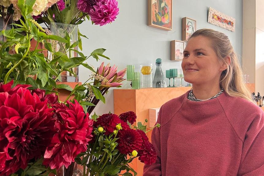 A blonde woman smiles and looks at a floral display