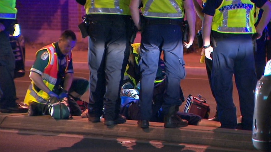 A paramedic on the ground with police officers facing away from the camera