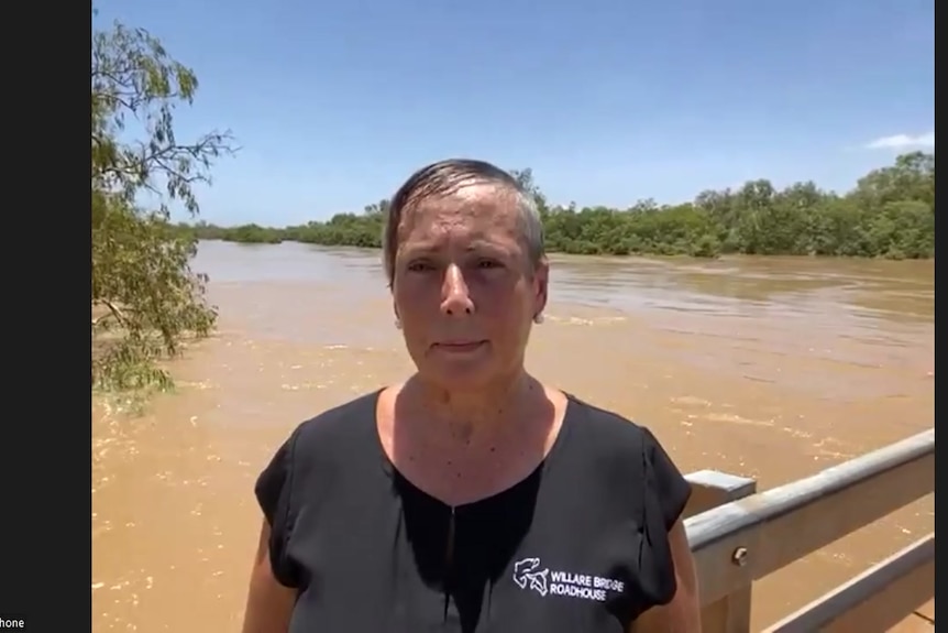 Neralie standing in front of a flooded muddy brown river 