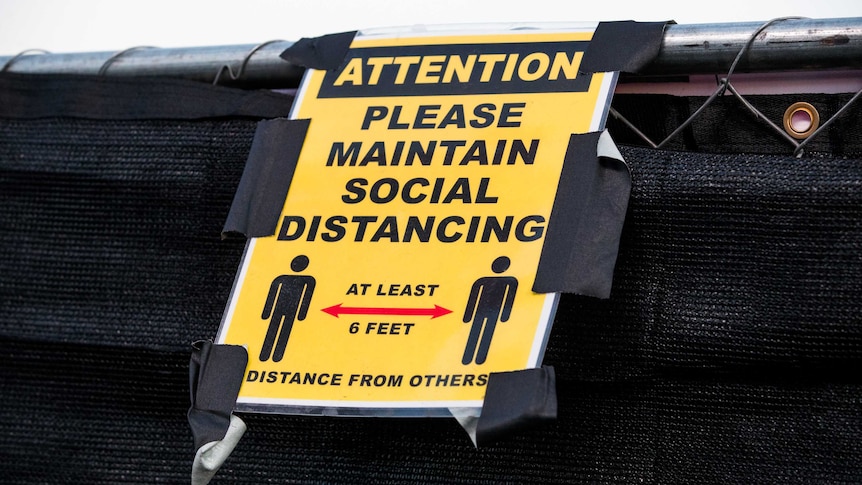 A yellow sign telling people to maintain distance is mounted on a black event fence.
