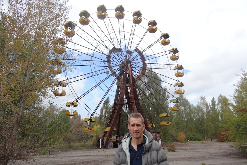A man stands in front of an ageing ferris wheel. 