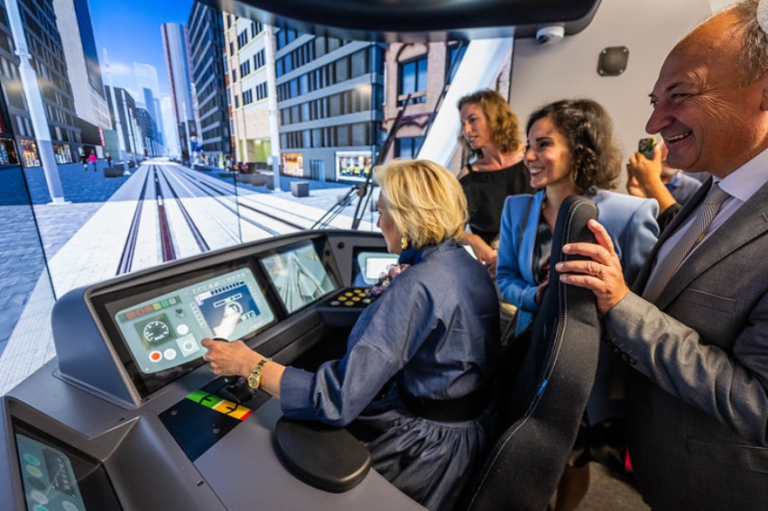 A woman sits in a light rail simulator cabin surrounded by other people 