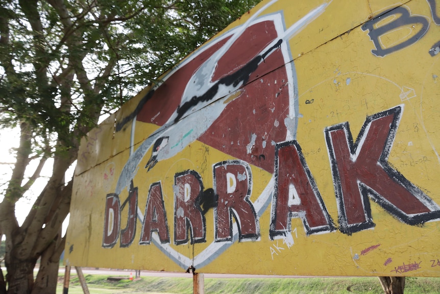 A yellow and maroon Djarrak football club sign with a bird drawn above the writing.