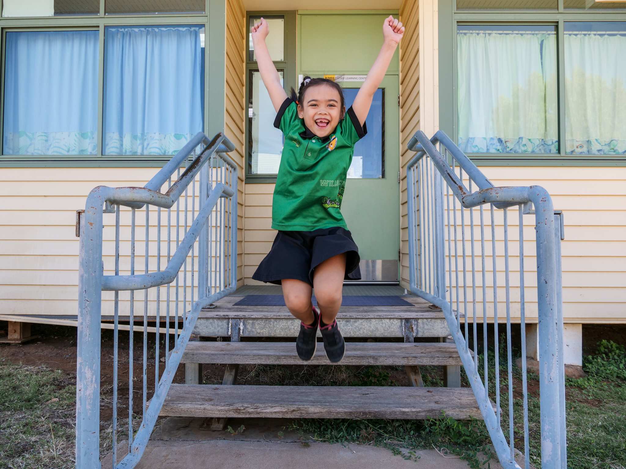 A young girl jumps off a stair with her arms and legs in the air. She is smiling widely.