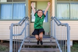 A young girl jumps off a stair with her arms and legs in the air. She is smiling widely.