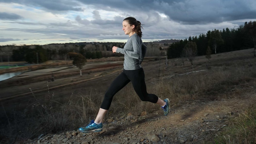 A woman running on a narrow trail.