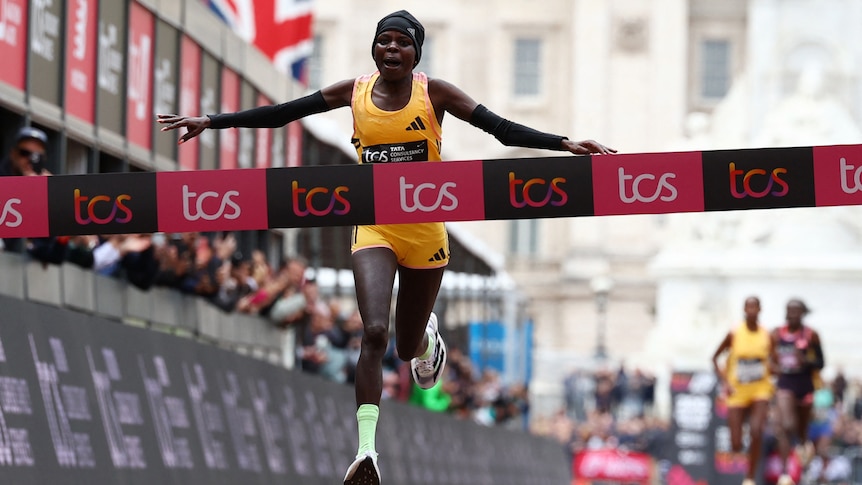 A professional runner crosses the finish line first, with her arms outstretched in celebration