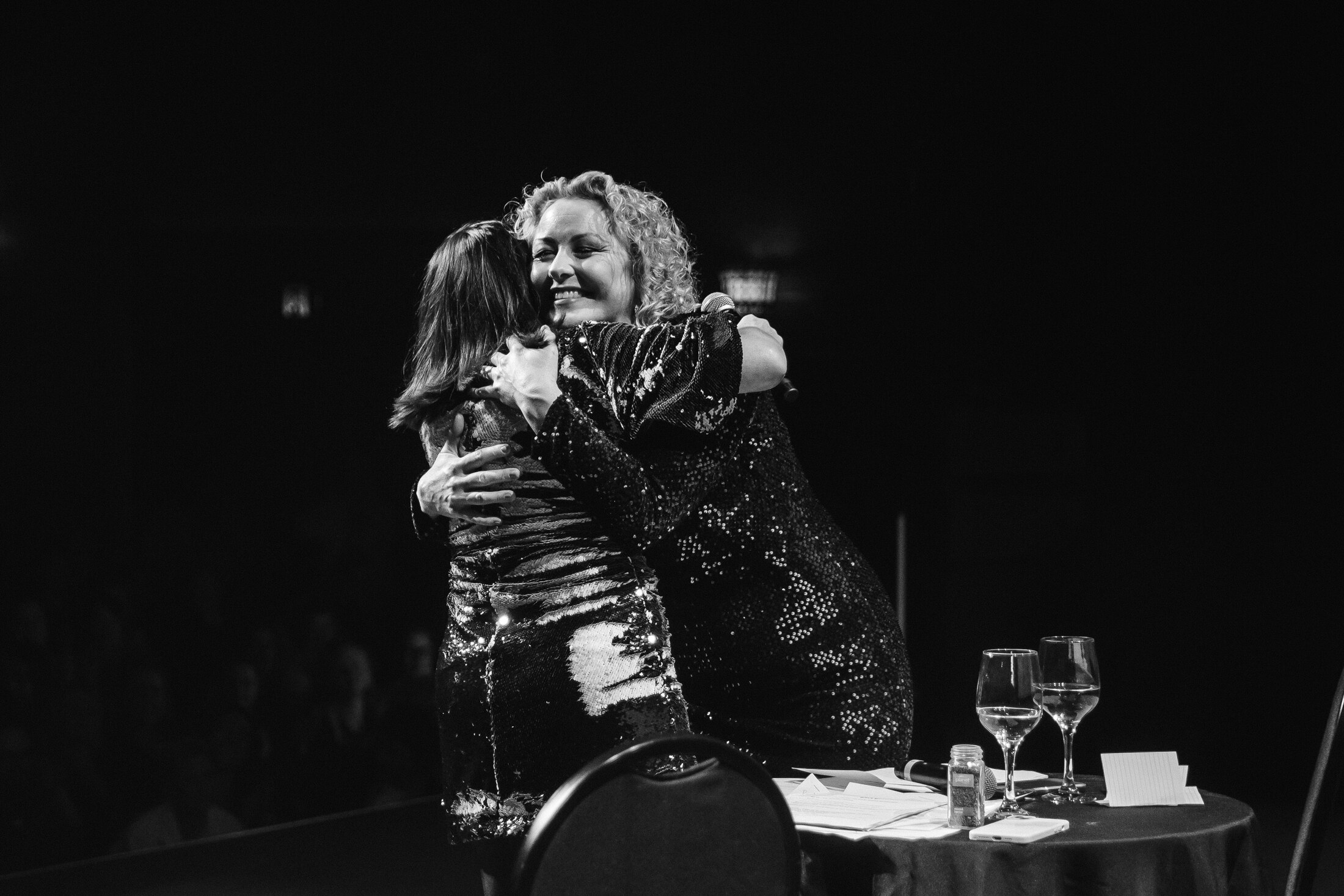 Black and white image of Myf and Zan hugging on stage at Bang On Live