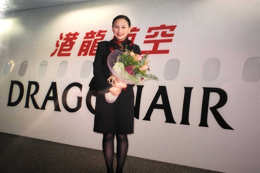 Rebecca Sy stands in front of a Dragonair plane, holding a bunch of flowers.