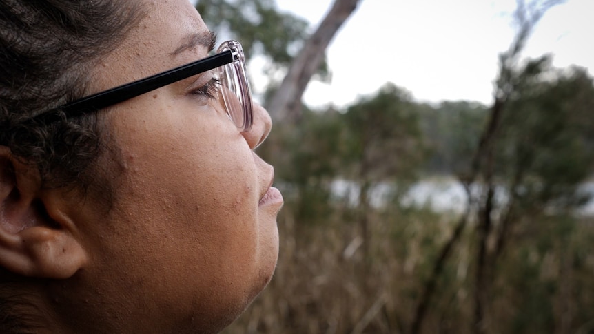 Side shot of young woman in glasses with meditative expression looking out at a wetland.