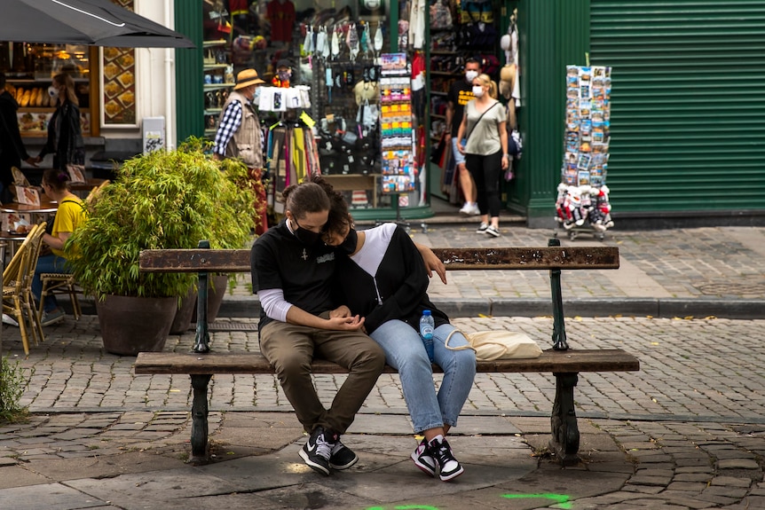 A couple, both wearing face masks to fight against the spread of the coronavirus, sit on a bench in downtown Brussels.