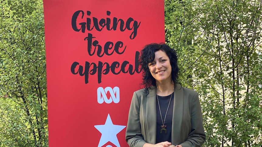 Woman with black curly hair smiling at camera, with a banner that reads Giving Tree Appeal
