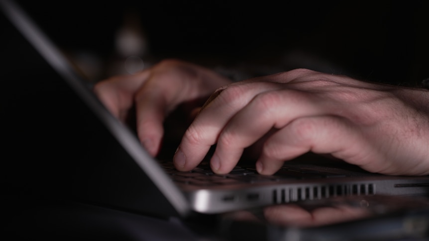 Unidentified male using laptop in dark environment.