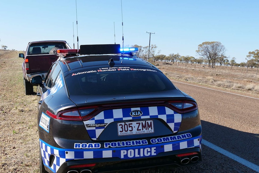 A dark blue police car pulls over a motorist in outback Queensland.