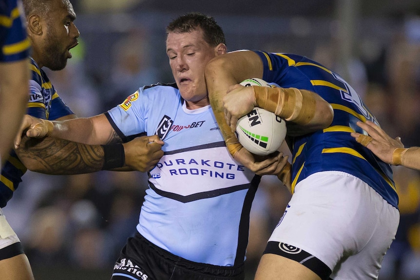 Paul Gallen grimaces while fending one Eels tackler off and wearing an elbow to the face from another.