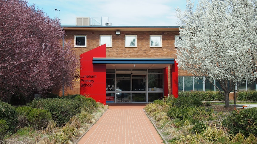 A building with a red entrance and tree-lined path out front.