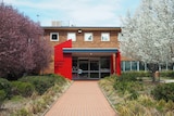 A building with a red entrance and tree-lined path out front.