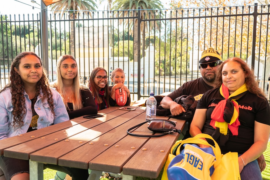 An Indigenous family sitting at a table wearing footy gear ahead of the Long Walk in Perth.  