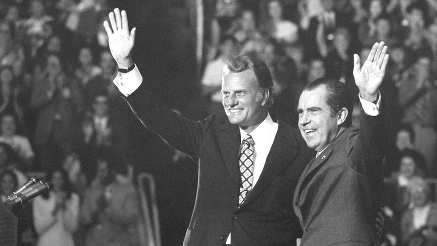 Billy Graham and Richard Nixon wave to a crowd in a black-and-white image.