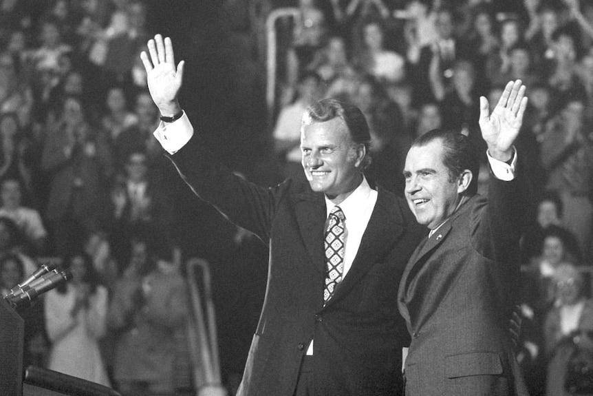 Billy Graham and Richard Nixon wave to a crowd in a black-and-white image.