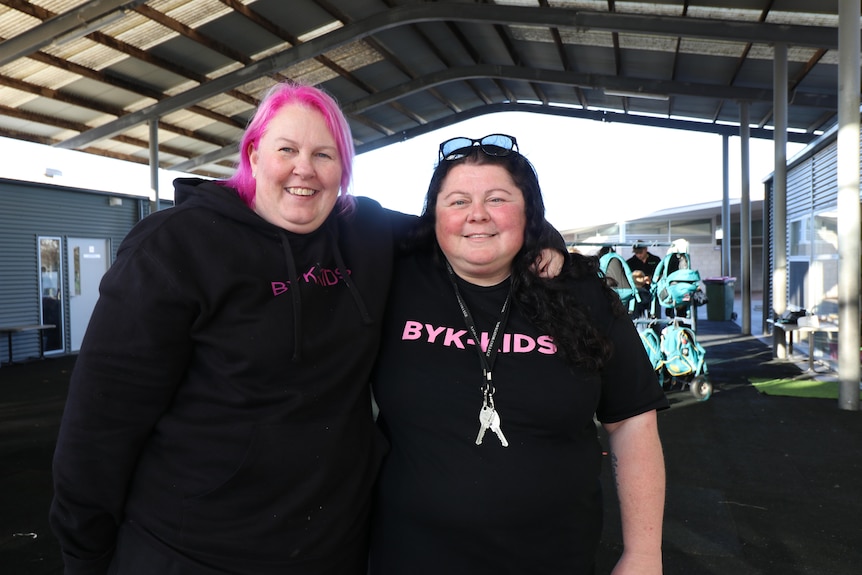one woman with pink hair and a woman with brown hair stand next to each other smiling