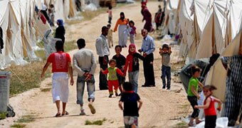 Syrian refugees walk past tents.