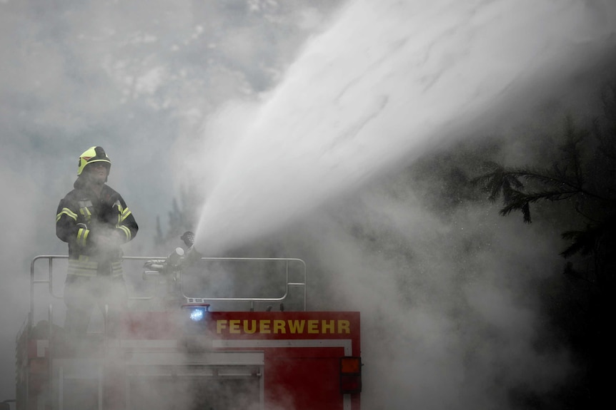 A firefighter engulfed in smoke sprays a hose at the fire