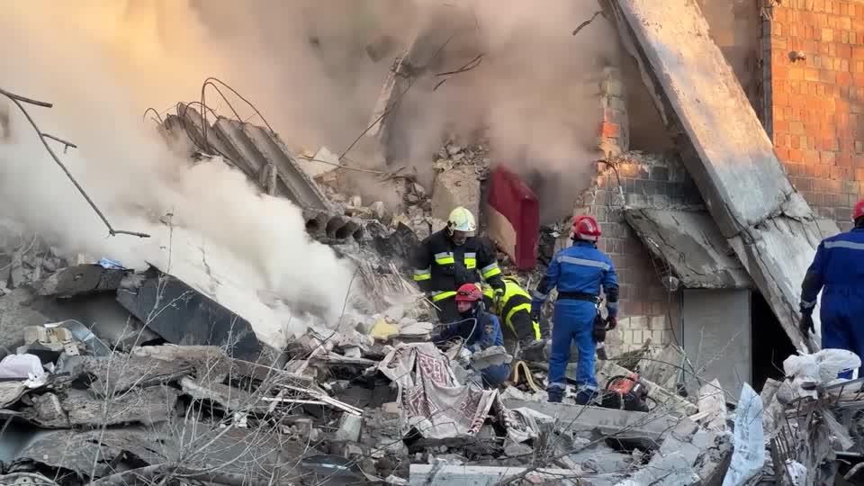 Emergency services workers examine smoking rubble.