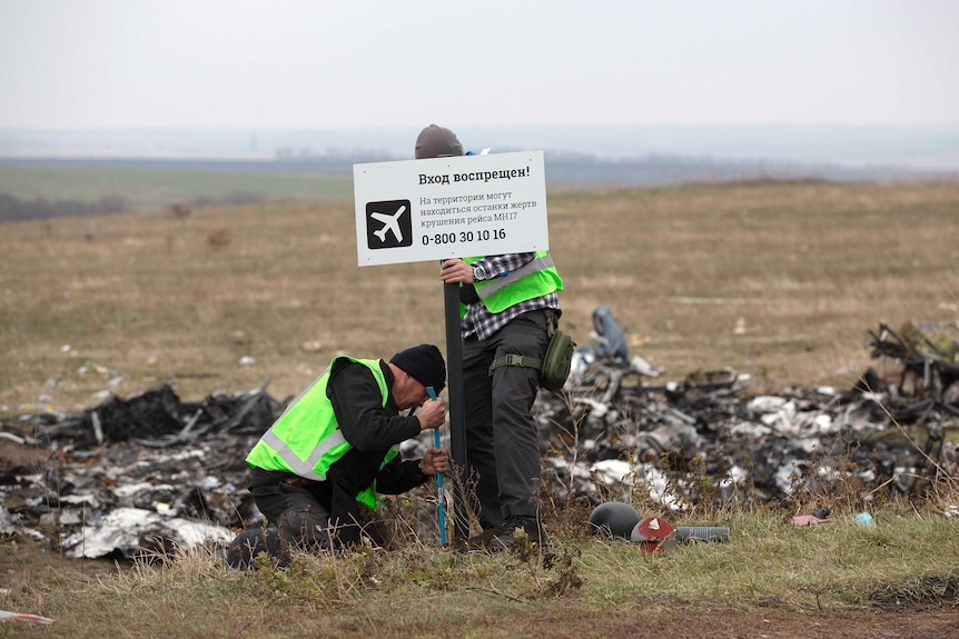 Dutch investigators place a sign near parts of flight MH17 at the crash site.