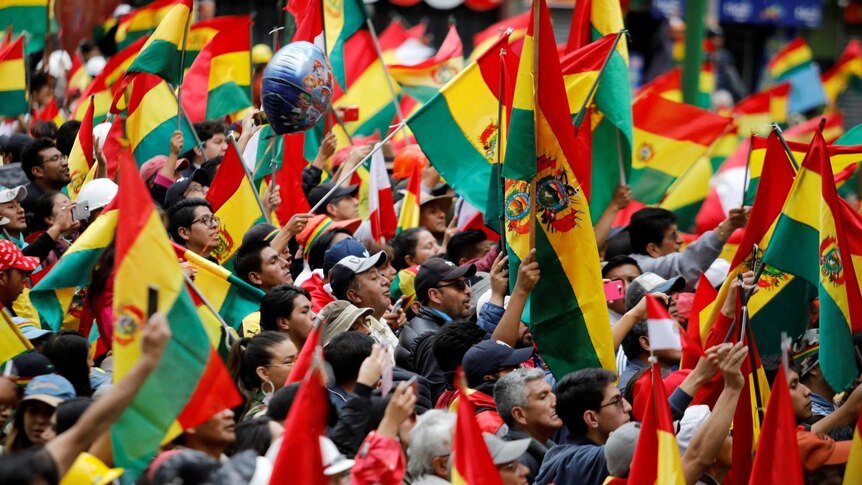 A large crowd wave Bolivian flags in the air.