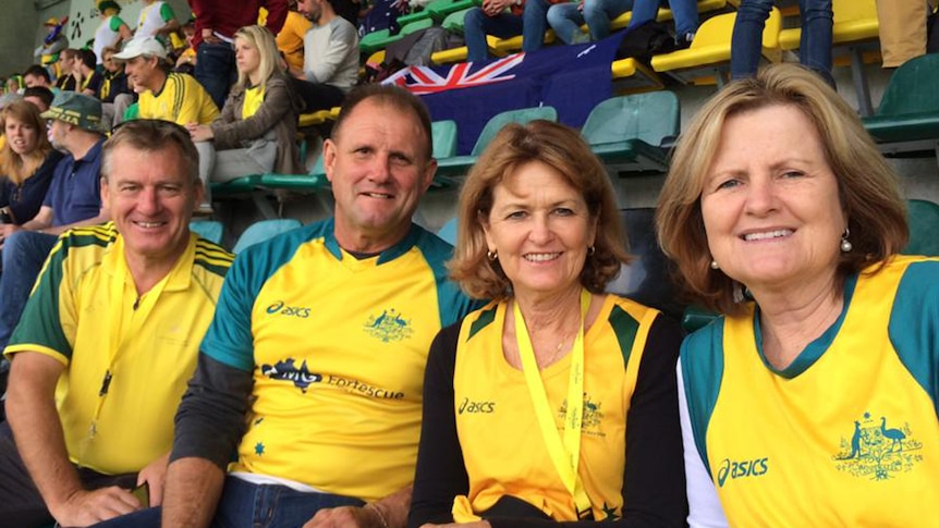 Barry Dwyer, Geoff Gohdes, Lea Dwyer and Kim Gohdes sit next to each other in a grandstand wearing gold and green colours