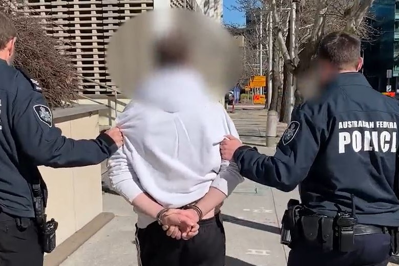 A handcuffed man being led by two police officers.