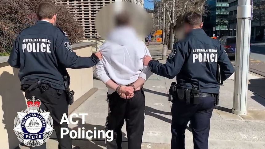 A handcuffed man being led by two police officers.