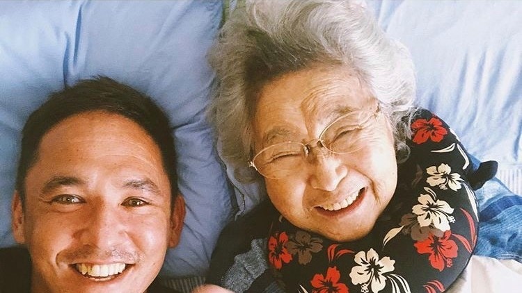 A selfie of a young man and  an elderly woman, who is pointing at the camera