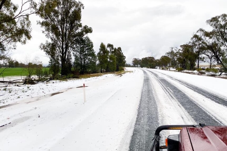 A road stretches ahead completely covered in white from a hail storm, with dark clouds on the horizon