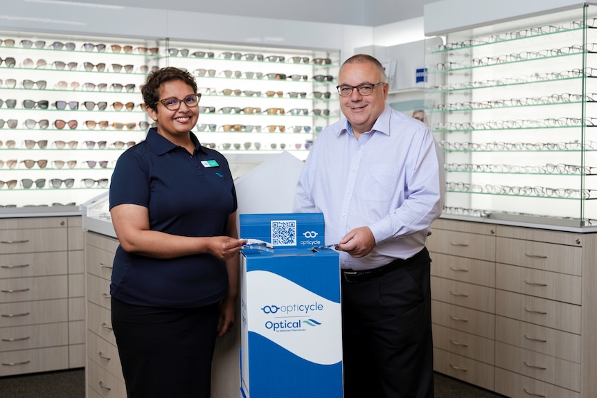Two people with a box for recycling contact lenses.