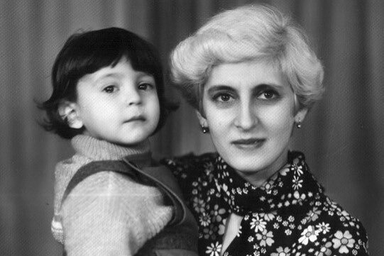 A black and white photo of a toddler-aged Volodymr Zelenskyy in the arms of a woman with cropped blonde hair